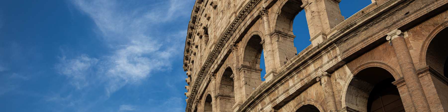 The sun shines behind the colosseum in Rome during mid-day.